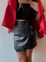 Minifalda negra de ecocuero con diseño cruzado y detalle de argollas metálicas.