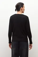 Cardigan negro de tejido fino, con escote en V y cierre frontal de botones plateados. Presenta aberturas en los puños.