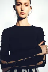 Top ajustado de punto acanalado color negro, de cuello redondo y manga larga con aberturas y botones metálicos en los brazos.