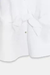 Camisa de lino en color verde militar, con cuello solapa y mangas muy cortas con terminación en vuelta. Presenta un detalle de nudo en la parte delantera y cierre frontal con botones metálicos.