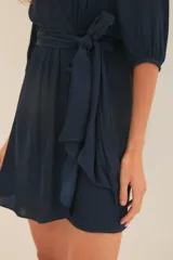 Vestido corto azul marino de manga 3/4, con escote en V cruzado y lazo en la cintura.