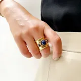 Anillo ancho de bronce con acabado martillado y tres piedras naturales engarzadas: una central grande de lapislázuli y dos laterales más pequeñas de piedra oscura.