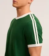 Remera de algodón de corte regular, color blanco hueso, con cuello redondo y ribete negro. Presenta un diseño de doble raya negra en las mangas y ribetes negros en el cuello y los puños de las mangas.