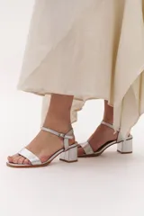 Sandalias plateadas de cuero con taco bajo cuadrado y tira fina con hebilla en el tobillo.