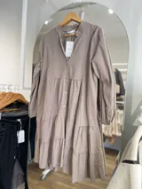 Vestido marrón claro de pana con cuello mao, corte evasé, mangas largas con puños elásticos y falda escalonada con volantes.