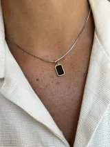 Collar con cadena de eslabones tipo caja plateada y un dije rectangular con borde plateado y centro de piedra negra pulida.