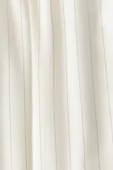 Pantalón de sarga color crudo con finas rayas verticales en gris, de tiro alto con cintura elástica y cierre decorativo. Tiene bolsillos laterales discretos y piernas anchas con pliegues cosidos adelante y pliegues planchados atrás.