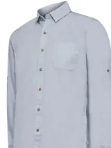 Camisa celeste de manga larga con cuello camisero, cierre con botones de madera y bolsillo en el pecho.