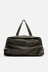 Bolso de viaje marrón oscuro fabricado en piel con acabado craquelado. Tiene un compartimento principal con cierre de cremallera, un bolsillo plano interior con cremallera y dos bolsillos frontales con botón a presión. Cuenta con asas de mano de piel y asa de hombro removible y ajustable.