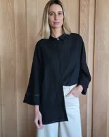 Camisa negra de corte amplio, con cuello clásico, cierre frontal con un botón y mangas 3/4 con detalle de costuras en puños y ruedo.