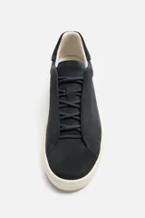 Zapatilla deportiva de hombre color gris topo, fabricada en piel con acabado serraje. Presenta cordonera elástica oculta y suela de goma de bajo volumen.
