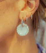 Aros colgantes con forma circular, hechos de resina color lila y borde de strass plateado. El aro es de acero quirúrgico plateado.