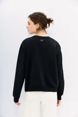 Buzo negro de algodón con cuello redondo y mangas largas. Presenta apliques bordados de piedras brillantes en forma de flores y otros motivos decorativos en el frente.