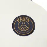 Buzo de entrenamiento Nike del Paris Saint-Germain, modelo Strike. Color crema con detalles en azul marino en cuello y hombros. Cuenta con cierre corto en el cuello, logo de Nike bordado en el pecho y escudo del PSG.