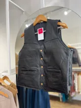 Chaleco negro de cuero con diseño de paneles geométricos y botones dorados.