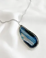 Collar con cadena de acero plateado y dije de piedra ágata natural con vetas azules, blancas y negras, con borde plateado.