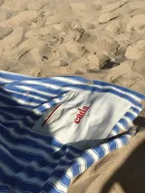 Lona de playa a rayas azules y blancas con un bolsillo central de color crudo bordado con la palabra "cada." en rojo.