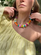 Collar corto con cuentas de resina y cerámica de colores naranja, rosa, verde, celeste y beige. Tiene tiento sintético con cierre ajustable.