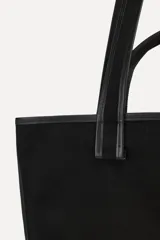 Bolso tipo tote confeccionado en algodón color negro, con doble asa y detalle de parche con el logo "50" y la leyenda "A Coruña".
