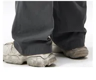 Pantalón cargo negro de corte ancho, confeccionado en gabardina de algodón. Presenta cintura elástica y regulable con cordón blanco, y múltiples bolsillos cargo laterales con costuras destacadas.