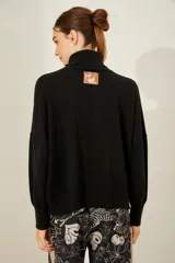Sweater negro oversize de tejido de punto, con cuello alto y detalle de costuras a la vista.