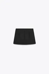 Falda pantalón corta negra de tiro alto con cinturón del mismo tejido y hebillas metálicas. Cierre trasero con cremallera oculta.