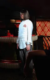 Remera blanca de manga larga superpuesta a una camisa blanca de manga larga, ambas con cuello. La prenda exterior tiene un estampado frontal en naranja con texto censurado inspirado en la película Pulp Fiction.