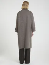 Tapado largo de paño texturado color gris topo, de corte oversize y doble botonadura. Presenta cuello con solapas anchas y mangas largas con puños doblados.
