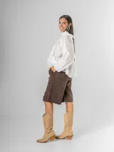 Camisa blanca de algodón italiano con cuello alto ajustable mediante lazo trasero, mangas abullonadas y un gran shabot frontal con volados en cascada.