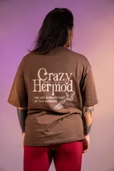Remera oversize marrón de algodón elastizado con estampado en la espalda que incluye el texto "Crazy Hermod movement" y un diseño de zapatilla alada.