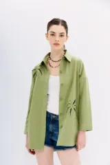 Campera recta color verde claro confeccionada en gabardina, con cuello camisero, mangas largas y bolsillos ojal. Presenta bordados calados en forma de palmeras en el frente y la espalda.