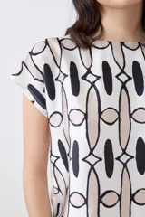 Blusa de manga corta con estampado geométrico en tonos beige, blanco y negro.