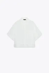 Camisa blanca de cuello solapa y manga corta, con bolsillo delantero y detalle de vainicas a tono. Cierre frontal con botones ocultos por solapa.