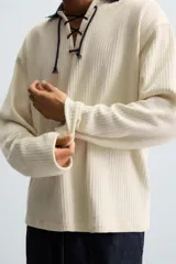 Sudadera color crema de tejido con estructura vertical, corte relaxed fit, cuello polo combinado en color azul marino y ajuste frontal con cordón.