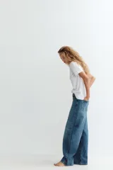 Jeans de tiro medio color azul denim, corte baggy, con trabillas y cinco bolsillos. Cierre frontal asimétrico con cremallera y botones metálicos.