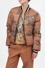 Campera puffer color camel con estampado de paisaje en azul marino, cuello y puños tejidos con rayas blancas y negras. Impermeable.
