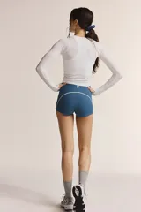 Top deportivo de manga larga, color blanco, con cuello redondo y detalle fruncido ajustable en el centro del busto.