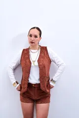 Chaleco marrón de gamuza sintética con apliques de flores y tachas doradas.