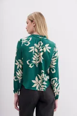 Camisa holgada verde esmeralda con estampado floral en color crema, escote redondo con abertura frontal y lazo de ajuste, mangas largas con puños elastizados con volados.