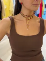 Collar de dos vueltas con bastones cilíndricos dorados y cuentas de piedra roja irregular intercaladas. El diseño cae en forma de 'Y' con un dije de cristal transparente en la punta.