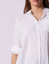 Camisola larga de algodón color blanco, marca Dash. Tiene cuello con solapa, abertura central con botones, bolsillo aplicado en el pecho, mangas regulables con presilla y botón, y bolsillos laterales en la costura.