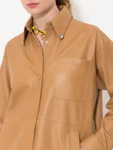 Camisa color camel confeccionada en cuero ovino, con remaches brillantes en las puntas del cuello y cierre con broches forrados en cuero.