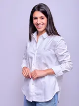 Camisa blanca de algodón, corte holgado, con cuello clásico y botones frontales. Las mangas son largas y se ven remangadas.