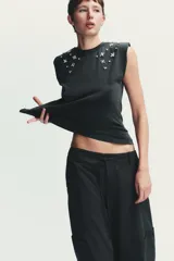 Camiseta negra con efecto lavado, cuello redondo, sisas amplias con hombreras y apliques de joyas combinadas a contraste en la parte superior.