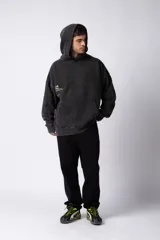 Buzo canguro negro con capucha, de corte oversize y estética lavada. Presenta un bolsillo tipo canguro y puños con orificio para el pulgar. Estampado con texto en el lateral izquierdo.