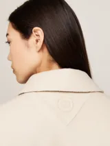 Gabardina corta color crema de Tommy Hilfiger confeccionada en mezcla de lana sostenible. Tiene cuello inglés, botonadura sencilla, monograma TH en relieve en la nuca y logo metálico en el puño.