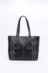 Cartera tote negra de símil cuero con bordados decorativos en color beige, inspirados en el estilo western. Tiene asas largas para llevar al hombro.