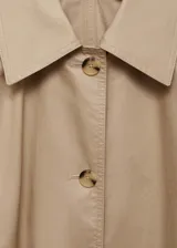 Abrigo largo color beige con cuello camisero, cierre frontal con botones, lazo ajustable en la cintura, trabillas, bolsillos laterales y forro interior.