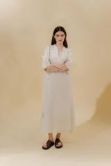 Vestido largo color beige, confeccionado en lino, con escote en V con volados y apliques de puntilla en las mangas. Posee bolsillos delanteros y tajos laterales.