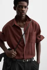Camisa color borgoña de corte relajado, confeccionada en tejido con mezcla de viscosa. Tiene cuello solapa, manga larga con puños abotonados, bolsillo de parche en el pecho y cierre frontal con botones.